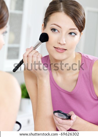 beautiful attractive woman applying eyeshadow with brush looking in the mirror