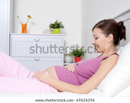 Happy pregnant young woman lying on the bed and touching belly