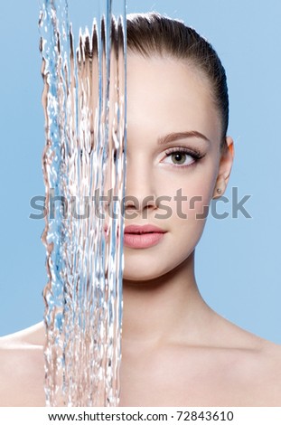 Stream of water falling before young beautiful clean face of teen - blue background