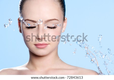 Beautiful young clean female face with splash of water - blue background