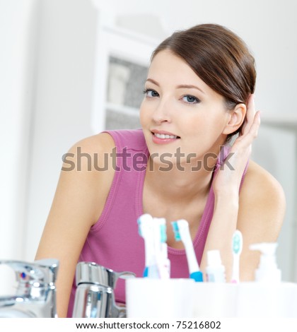 The beautiful smiling woman with clean skin face looking in mirror in a bathroom