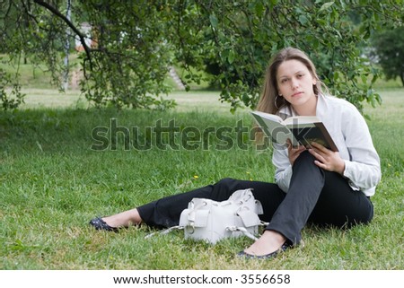 girl in white jacket with book sitting under the tree on grass