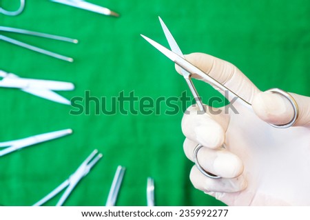 gloved hand holding a surgical scissors on the surgical drape sterile
