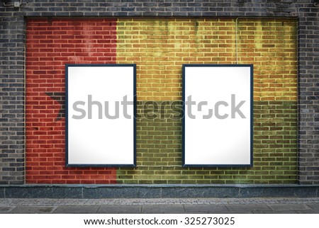 Two blank billboards attached to a buildings exterior brick wall which has a Guinea Bissau flag painted on it.