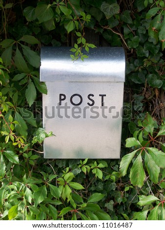 a metal postal box against a background of a hedge