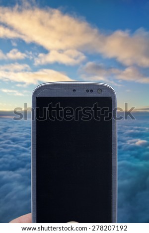 Smatrphone and cloudy sky. Idea for religious app, weather app, aerial transports, digital detox, taking shots, accessing apps, Internet, blogs and others. The blur image is a sky from Brazil