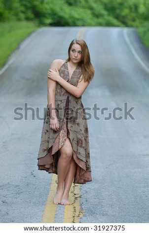 An attractive young woman standing alone in the middle of a street with a concerned expression on her face.