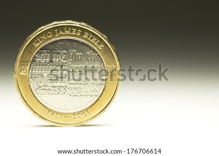 British Two Pound Coin with biblical engravings balancing on white surface. Finance and money concept