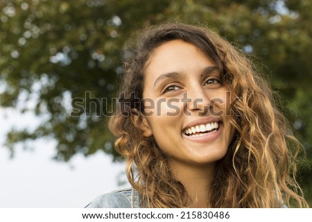 Portrait of an attractive young woman laughing at something past the camera whilst outdoors on a summer day
