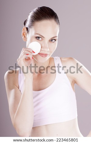 Sensual young woman cleaning skin with  cotton swab, over gray background. Skin care concept.