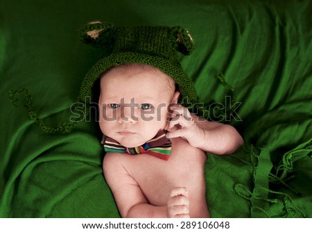 Cute newborn in a knitted hat with a bow tie lying on a green cloth.