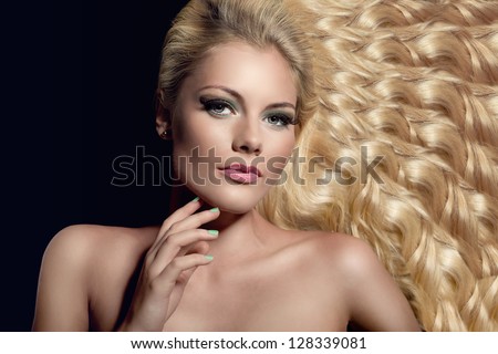 portrait of beautiful young blond woman with wavy hair and well done nails lying down on black background