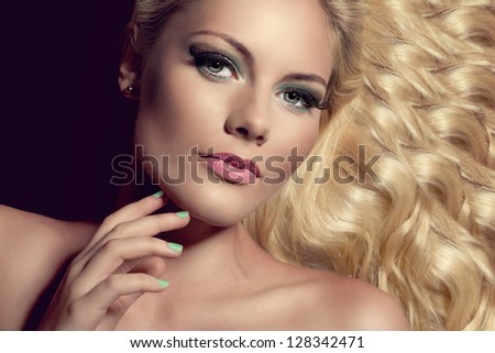 portrait of an attractive young blond woman with wavy hair and well done nails lying down on black background