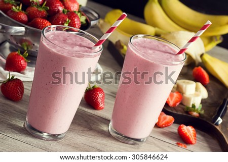 Two Cold Strawberry Banana Smoothies in Glasses with Ingredients on Kitchen Table