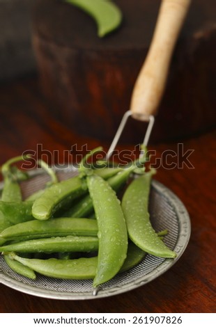 sugar snap pea with waterdrops in  colander on wooden background