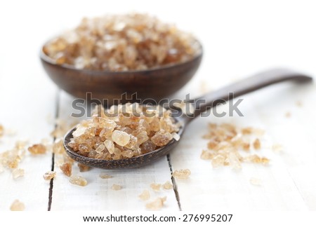 rock sugar in wooden spoon and wooden bowl on white wooden background