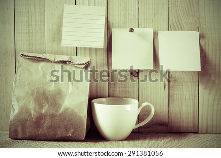 vintage colour style of paper bag of some food and coffee cup and note pad paper or note paper on wooden background. breakfast time with planing.