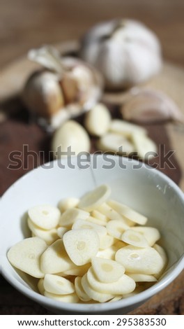 garlic slice in white ceramic cup, garlic clove, garlic bulb on chopping block made of a log