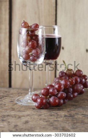 fresh grape in wine glass and glass of red wine on wooden background.