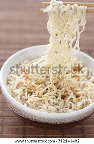 Instant noodles on chopsticks with flavored soup in bowl against white background. chinese noodle on chopstick. chopstick holding instant noodle.
