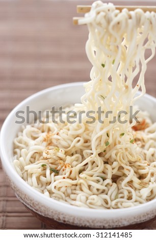 Instant noodles on chopsticks with flavored soup in bowl against white background. chinese noodle on chopstick. chopstick holding instant noodle.