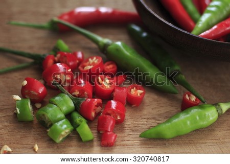 fresh red and green chilli and chopped fresh red and green chilli on wooden chopping block. guinea pepper ;bird pepper ; bird-chilli ; small capsicum ; chilli pepper ; tiny fiery chilli ; hot chilli .