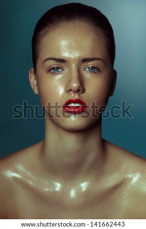Fashion portrait of fresh young girl with shiny skin coated with oil. Natural make-up, beautiful blue eyes, tied brown hair, white teeth and red gloss lips. Blue shaded background.