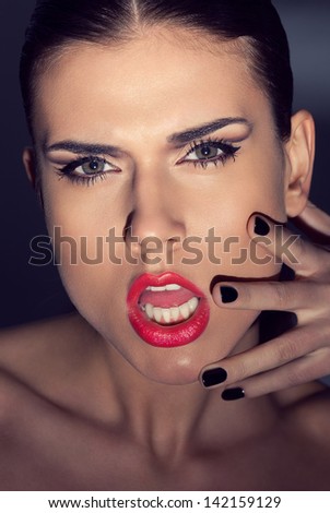 Fashion portrait of beautiful young woman with strong face expression. Touching her face with hand. Black nails manicure fashion makeup long black eyelashes red lipstick. Shaded background.