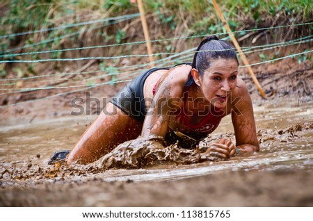 DALLAS, TEXAS - SEPTEMBER 15: Unidentified female participant crawls under the wires at a mud pit in the Dash of the Titans Mud Run Race on September 15, 2012 in Dallas, Texas.