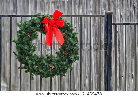 Christmas spruce fir wreath hanging on iron fence against gray background
