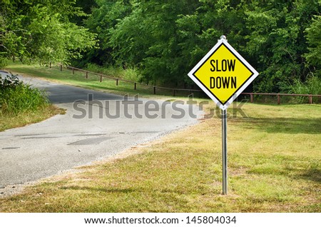 Slow Down yellow traffic sign on the roadside against green woods