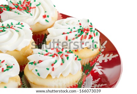 Holiday cupcakes with vanilla frosting and red and green sprinkles, served on a red holiday plate on white background with copy space. Shallow depth of field.