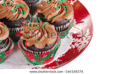 Holiday chocolate cupcakes with red and green sprinkles, served on a red holiday plate on white background with copy space. Shallow depth of field.