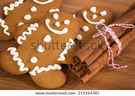 Freshly baked gingerbread man cookies with cinnamon sticks on wooden cutting board