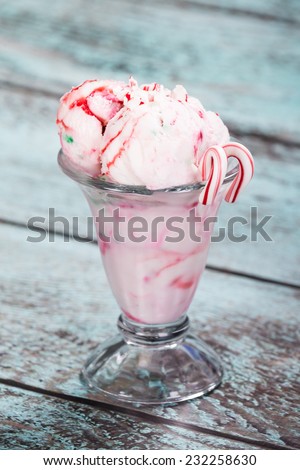 Peppermint ice cream with candy canes in a glass bowl, wooden vintage background
