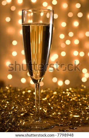 Champagne flute among golden ribbons, defocused lights background - shallow DOF, selective focus on the glass.