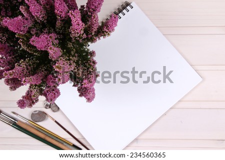 Open white and kraft notepads on the wooden table. Brush and flower. Mock up on the wood.