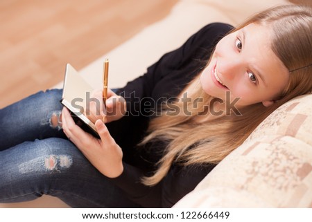 Happy teen writing to the diary sitting on the sofa in the living room
