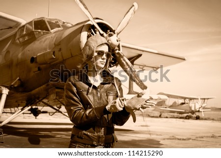 Portrait of beautiful female pilot with plane behind. Sepia photo.