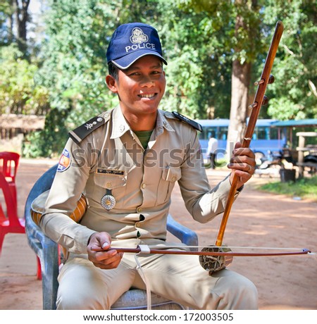SIEM REAP, CAMBODIA - NOV 21, 2013: Unidentified Policeman play on traditional cambodian musical instrument Thro khmer in Angkor Wat and collect money, on Nov 21, 2013 in Siem Reap, Cambodia.
