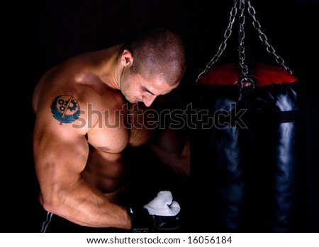 Attractive athletic young man training kickboxing using black punching bag