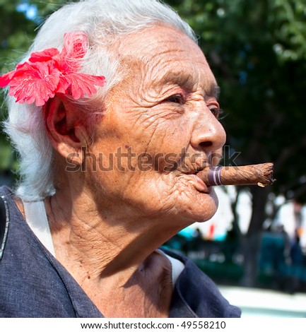 Old wrinkled woman with red flower smoking cigar. Santiago de Cuba, Cuba