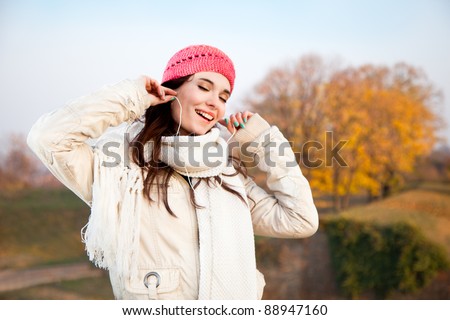 Beautiful happy woman listening music in autumn colored park