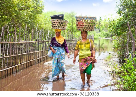 GILI MENO,INDONESIA- FEBRUARY 7: Two woman balancing food basket on the head while crossing fresh water lake on Gili Meno on February 7,2012 island Meno, Indonesia