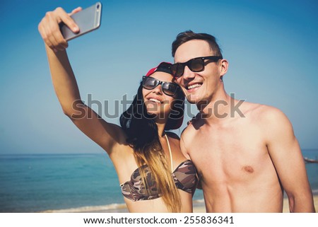 Happy beautiful multiracial couple of students in love doing selfie self-portrait photo on the beach, enjoy the holidays, sunbathe and have fun.