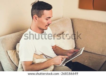 Man relaxing on the sofa and doing freelance work with a tablet at new home