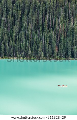 Kayakers on Lake Louise backdropped by a forest of giant fir trees in Banff National Park, Canada.