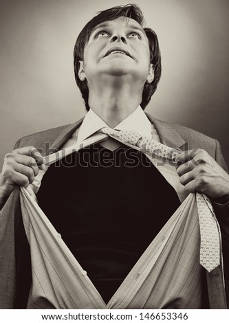 Business man tearing off his shirt over gray background. Monochrome portrait