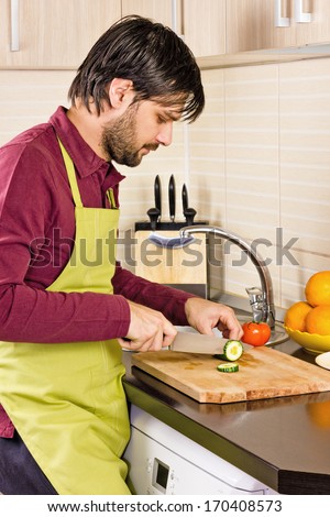 Handsome young man in the kitchen cutting vegetables on  wooden chopping board