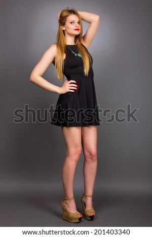 Full length portrait of sexy young blonde woman wearing a mini black dress against gray background